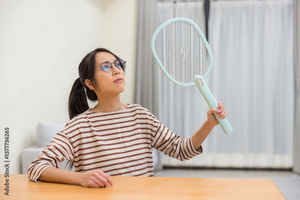 Woman killing mosquito with electric insect swatter at home