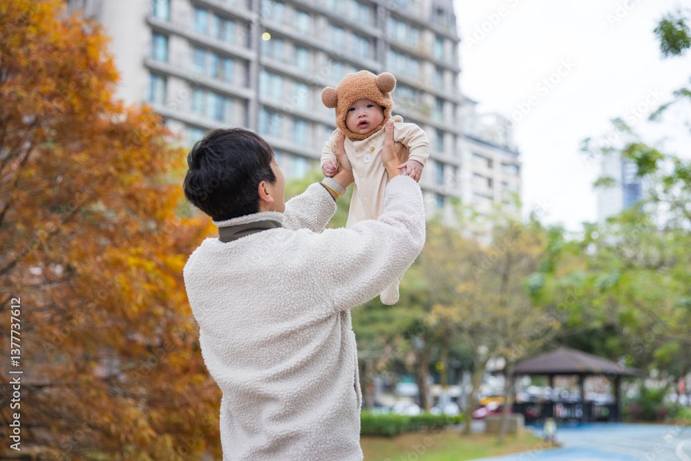 Dad holding baby up in city park