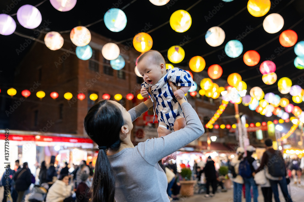 Mum lifting baby under many lanterns at outdoor