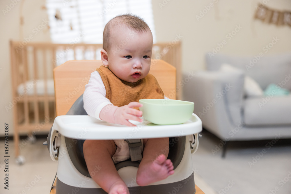Baby sitting in high chair holding bowl