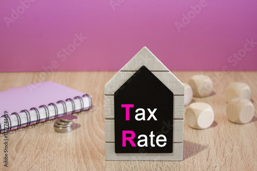 Text Tax rate on a black board. Beautiful purple background. Notebook and silver coins on the table. Business concept.