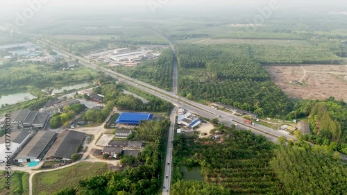 Aerial view of vibrant landscape showcasing highway, industrial buildings, palm trees, and water, highlighting harmony of nature and development amidst lush greenery.