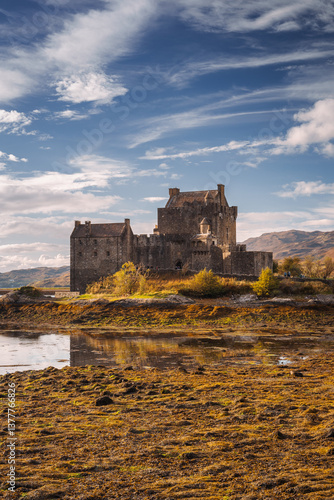 Obraz na płótnie Eilean Donan Castle stands majestically amid autumn hues, its reflection shimmering in calm waters. Misty Highlands and golden trees create a scene of timeless beauty. w salonie