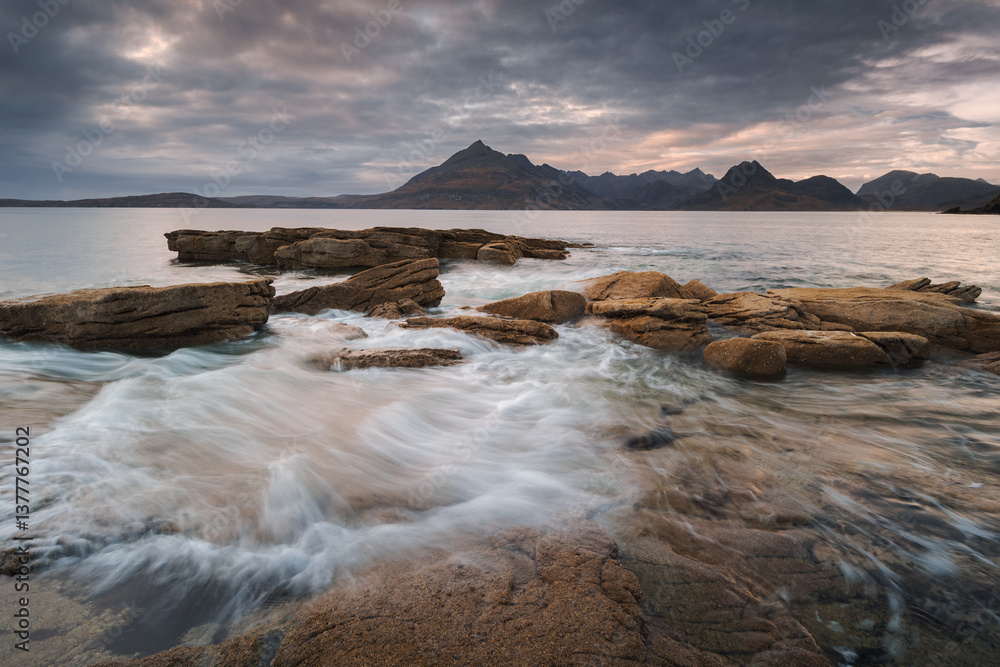 Dramatic waves crash against Elgol’s rugged coast, with the Cuillin Mountains rising in the misty distance. Autumn’s golden light enhances this wild, untamed beauty.