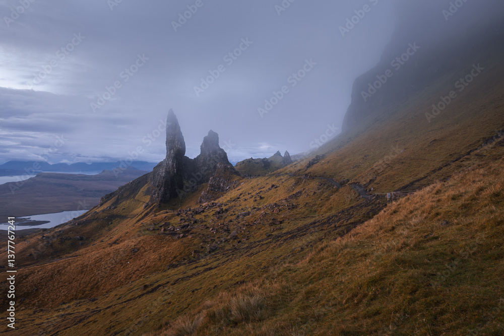 The Old Man of Storr emerges from autumn mist, its towering pinnacles glowing in golden morning light. A mystical, otherworldly Highland scene.