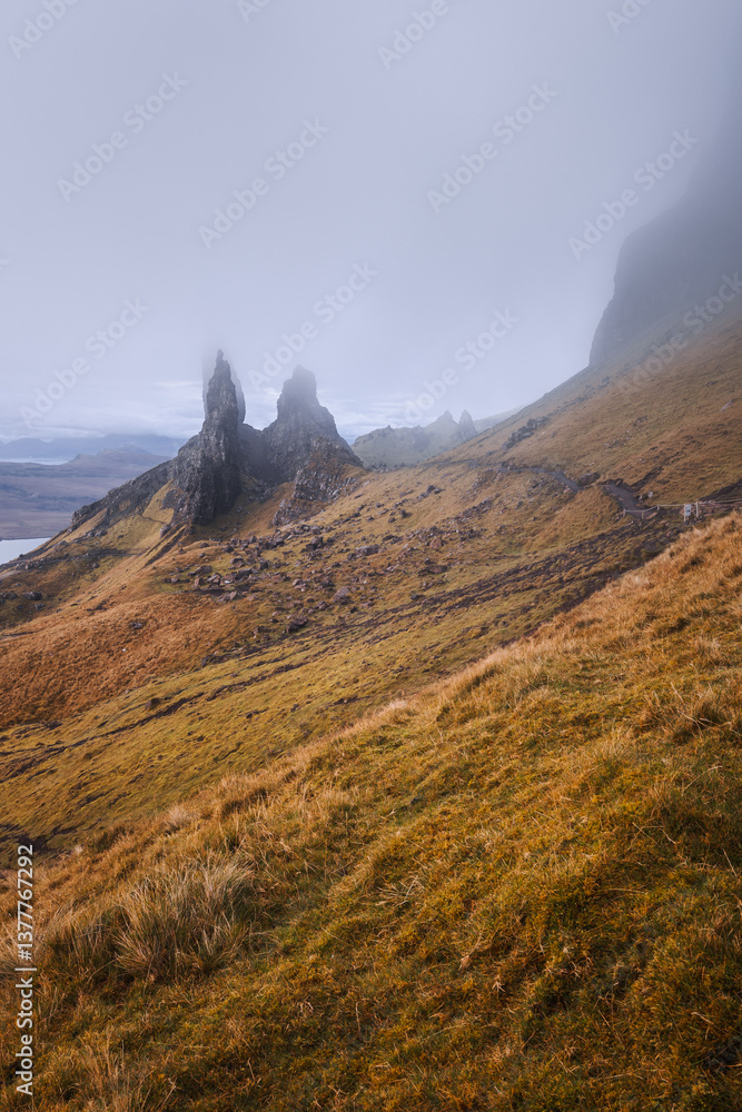 The Old Man of Storr emerges from autumn mist, its towering pinnacles glowing in golden morning light. A mystical, otherworldly Highland scene.