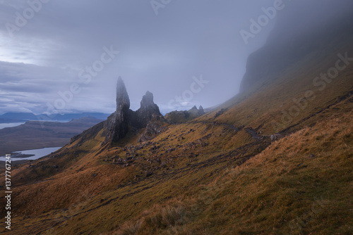 Obraz na płótnie The Old Man of Storr emerges from autumn mist, its towering pinnacles glowing in golden morning light. A mystical, otherworldly Highland scene. w salonie
