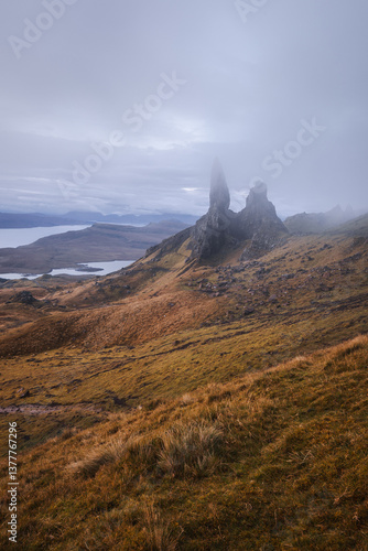 Obraz na płótnie The Old Man of Storr emerges from autumn mist, its towering pinnacles glowing in golden morning light. A mystical, otherworldly Highland scene. w salonie