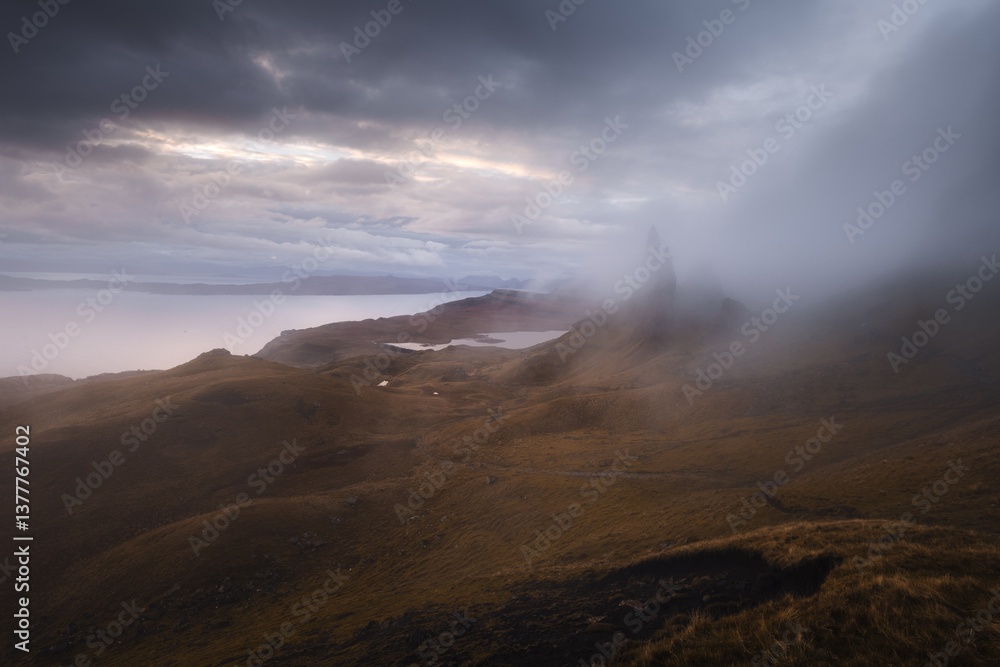 The Old Man of Storr emerges from autumn mist, its towering pinnacles glowing in golden morning light. A mystical, otherworldly Highland scene.