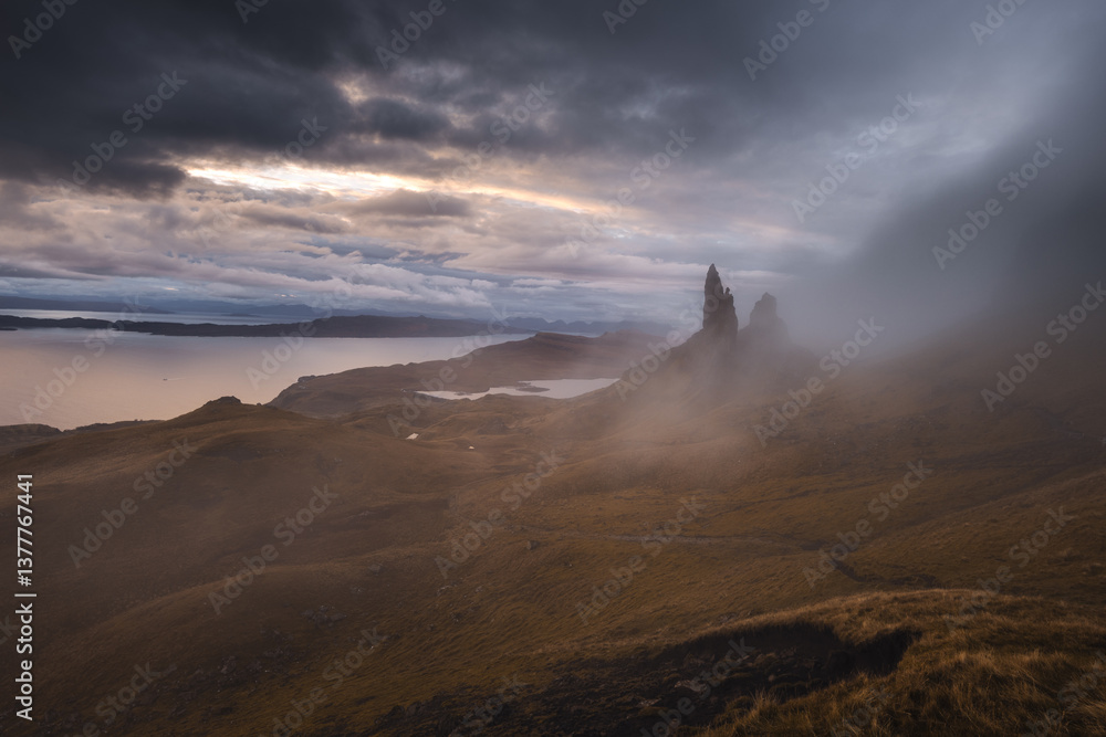 The Old Man of Storr emerges from autumn mist, its towering pinnacles glowing in golden morning light. A mystical, otherworldly Highland scene.