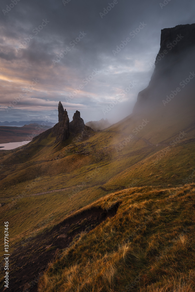The Old Man of Storr emerges from autumn mist, its towering pinnacles glowing in golden morning light. A mystical, otherworldly Highland scene.