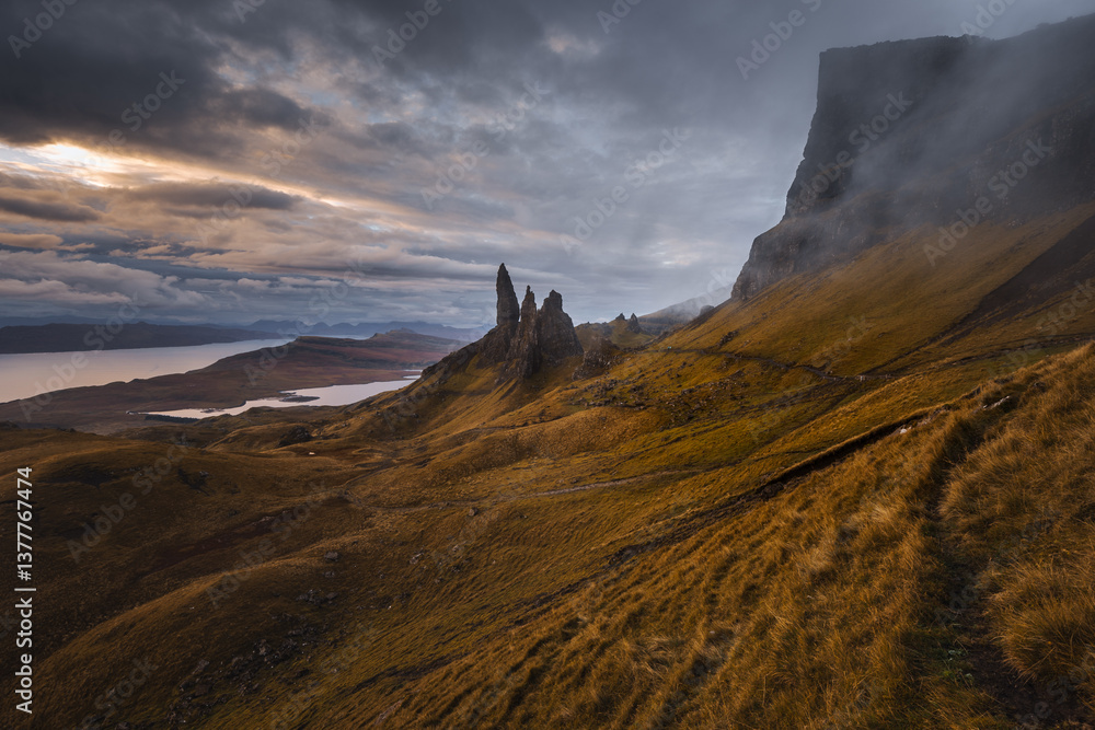 The Old Man of Storr emerges from autumn mist, its towering pinnacles glowing in golden morning light. A mystical, otherworldly Highland scene.