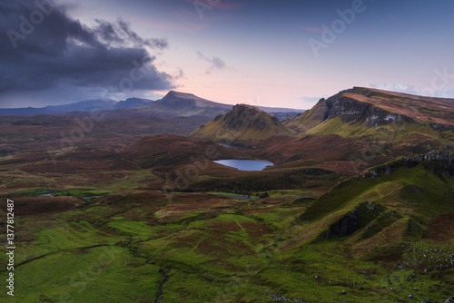 Autumn light bathes the Quiraing on Skye, casting long shadows over its dramatic cliffs and rolling hills. The landscape glows with golden hues, a breathtaking Highland scene.