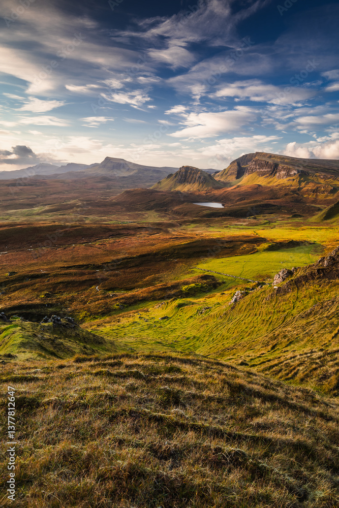 Autumn light bathes the Quiraing on Skye, casting long shadows over its dramatic cliffs and rolling hills. The landscape glows with golden hues, a breathtaking Highland scene.