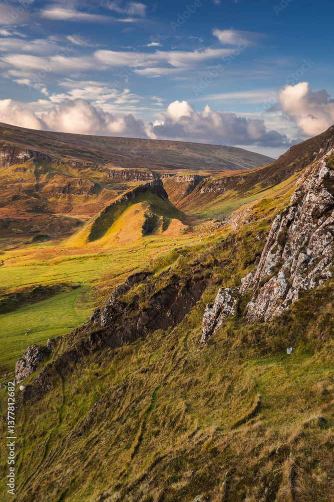 Autumn light bathes the Quiraing on Skye, casting long shadows over its dramatic cliffs and rolling hills. The landscape glows with golden hues, a breathtaking Highland scene.