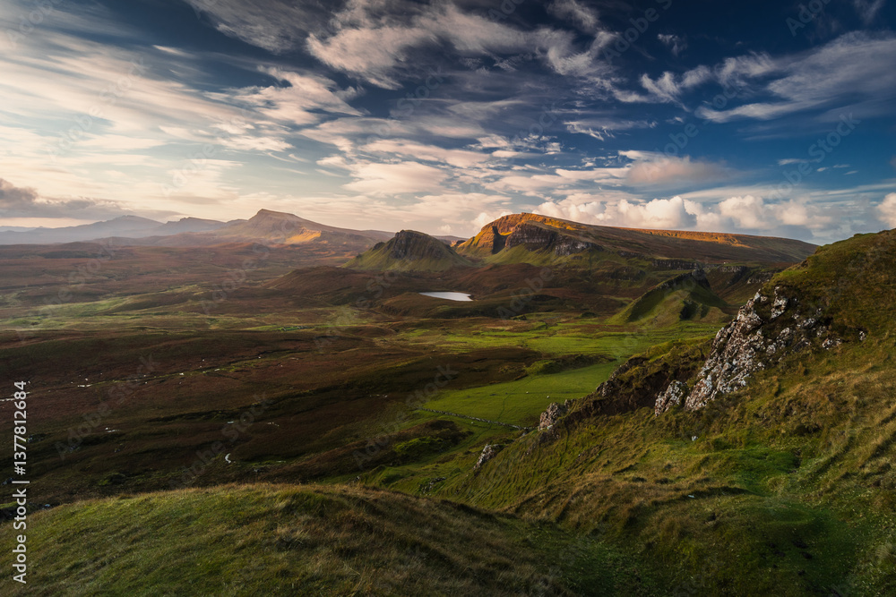 Autumn light bathes the Quiraing on Skye, casting long shadows over its dramatic cliffs and rolling hills. The landscape glows with golden hues, a breathtaking Highland scene.