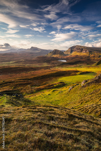 Autumn light bathes the Quiraing on Skye, casting long shadows over its dramatic cliffs and rolling hills. The landscape glows with golden hues, a breathtaking Highland scene.