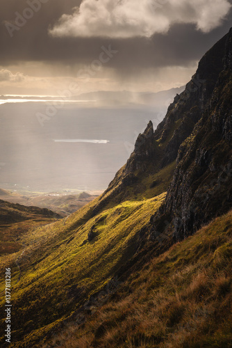 Autumn light bathes the Quiraing on Skye, casting long shadows over its dramatic cliffs and rolling hills. The landscape glows with golden hues, a breathtaking Highland scene.