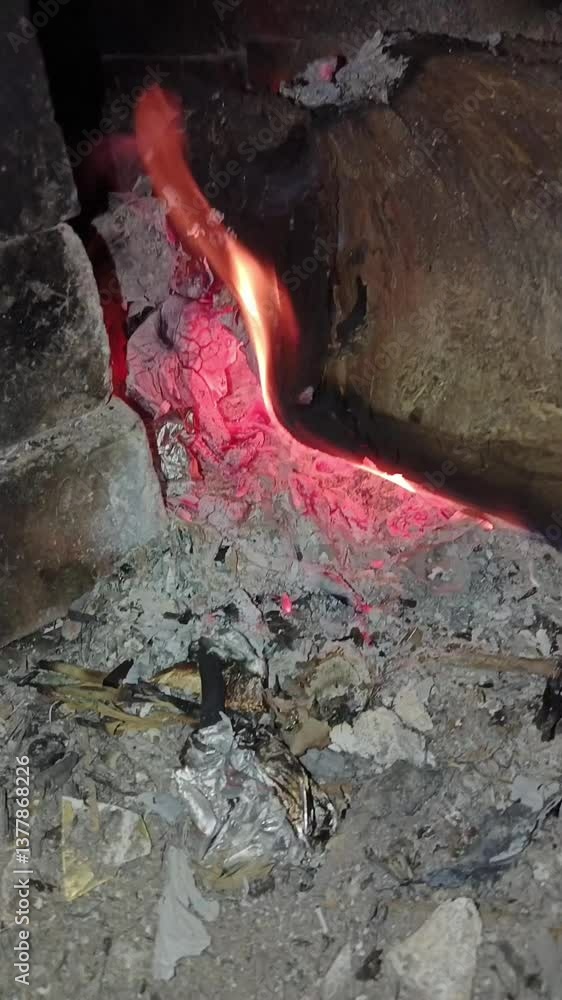 The wood burns slowly with glowing red embers, creating a warm and traditional atmosphere. Small flames creep among the ashes and charcoal, indicating the natural combustion process. The wood burns slowly with glowing red embers, creating a warm and traditional atmosphere. Small flames creep among the ashes and charcoal, indicating the natural combustion process.