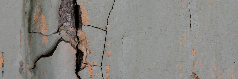 Peeling paint on the wall. Panorama of a concrete wall with old cracked flaking paint. Weathered rough painted surface with patterns of cracks and peeling. Panoramic texture for background and design.