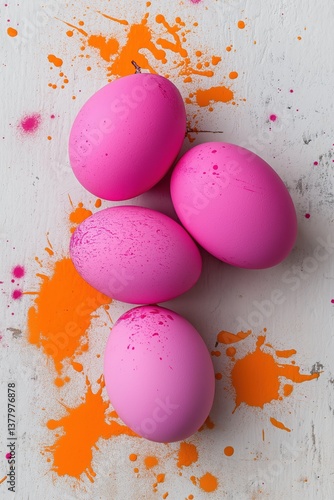 Four pink eggs are sitting on a table with orange splatters. The eggs are arranged in a pyramid shape, with the largest egg at the bottom and the smallest at the top