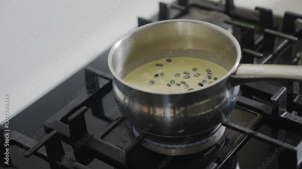 A metal pot filled with a thick, creamy substance sits on a stove burner. The stove is turned on, and the pot is bubbling and steaming. The substance appears to be a type of sauce or soup