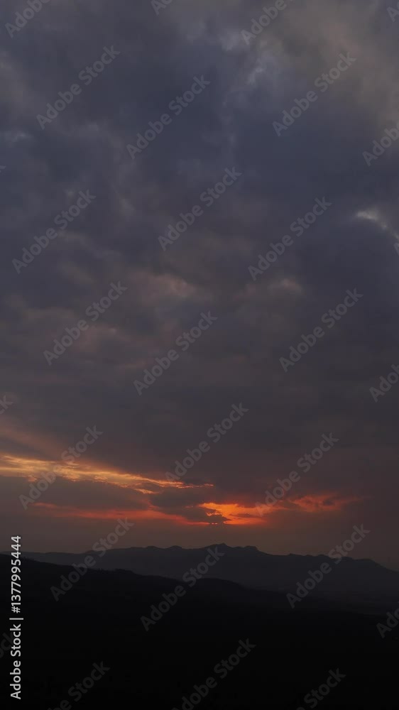A dramatic vertical cloudscape at sunset with vibrant red sunlight piercing through the horizon. A dramatic vertical cloudscape at sunset with vibrant red sunlight piercing through the horizon.