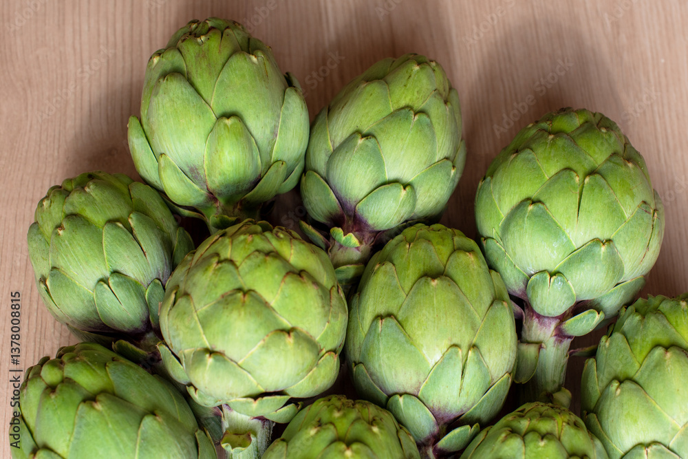 A detailed view of multiple green artichokes laid out on a table showcasing their texture. The image highlights the fresh, natural appearance of these vegetables, ideal for culinary, food, diet A detailed view of multiple green artichokes laid out on a table showcasing their texture. The image highlights the fresh, natural appearance of these vegetables, ideal for culinary, food, diet