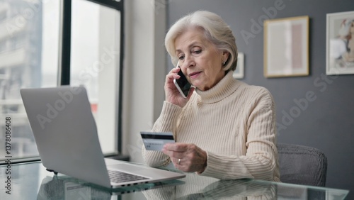 Older woman speaking on her cell phone while holding a credit card, possibly shopping or paying bills
