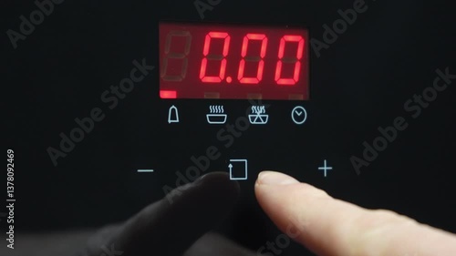 Close-up of a hand adjusting the digital display of a microwave oven. The index finger is setting a timer on the electronic panel, displaying the time in red.. High quality 4k footage