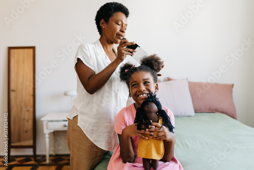 Black mother combing and caring for her daughter's hair in the bedroom