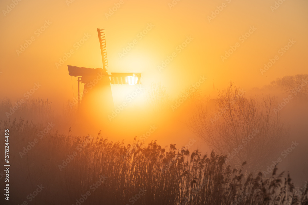 Sunrise at a Dutch, traditional windmill and a canal in the spring fog.