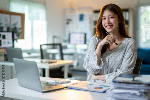 A woman is sitting at a desk with a laptop and a stack of papers