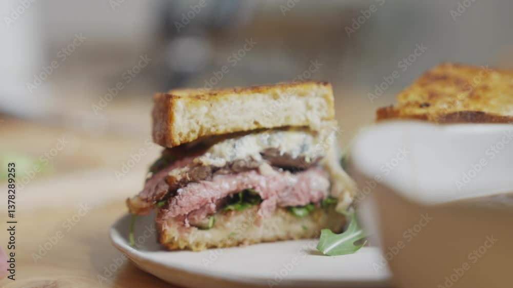 A sandwich is cut in half and placed on a white plate. The sandwich is made with meat and vegetables A sandwich is cut in half and placed on a white plate. The sandwich is made with meat and vegetables