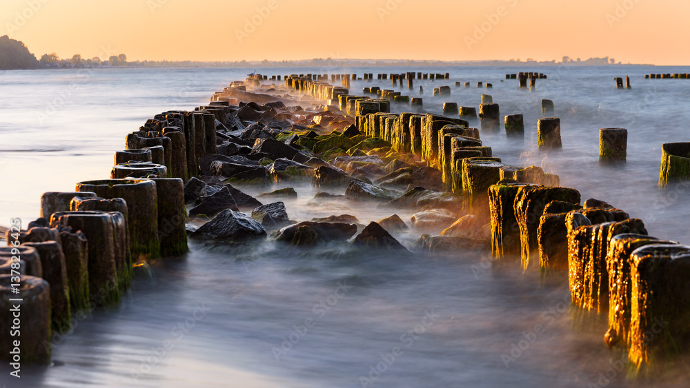 Obraz premium breakwater on the Baltic coast illuminated by the sun at golden hour.