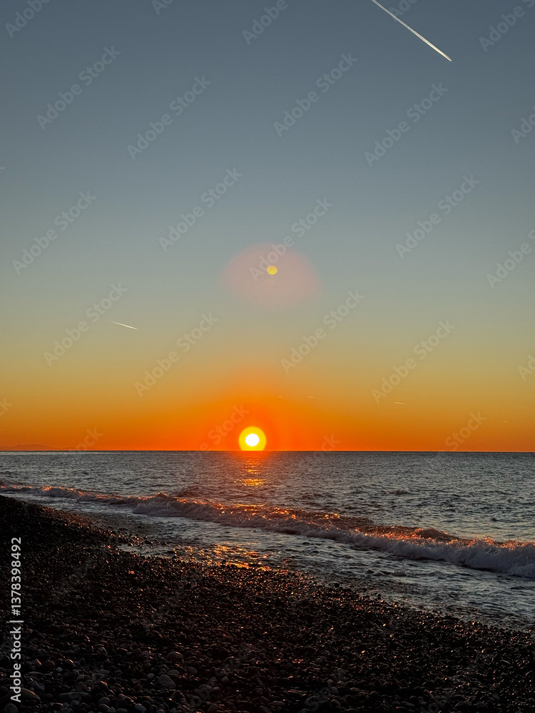 Sunset over pebble beach with ocean waves and sky contrails