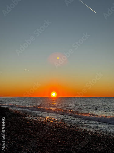 Sunset over pebble beach with ocean waves and sky contrails