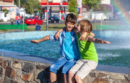 Two boys are sitting on a wall next to a fountain