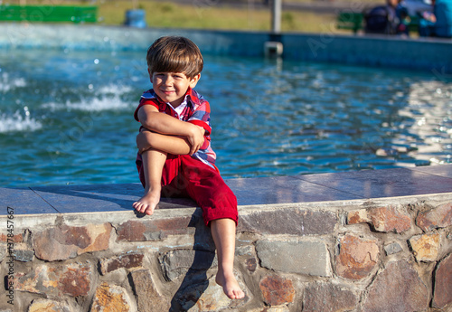 A boy is sitting on a ledge near a fountain