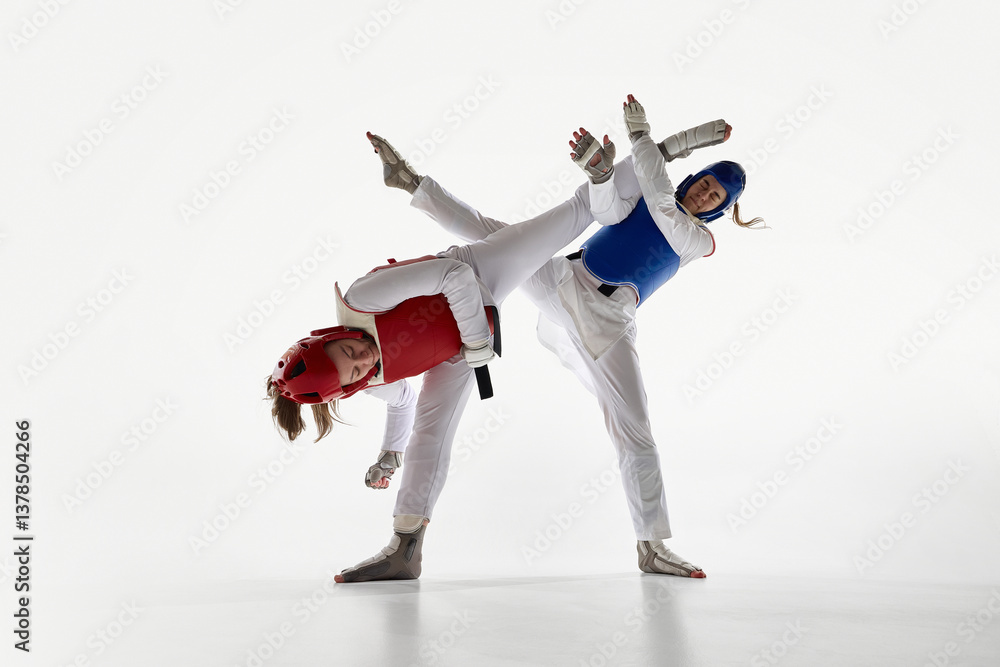 Fototapeta premium Two young women in blue and red taekwondo gear in dynamic motion, training against white background. Concept of martial arts, combat sport, strength, competition, power, endurance