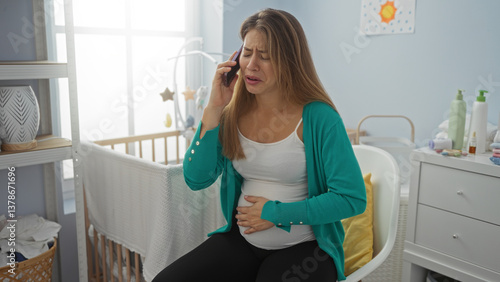 Woman talking on phone while sitting in bedroom beside cradle, looking worried, suggesting a home setting with an indoor scene, the atmosphere intimate yet stressful.