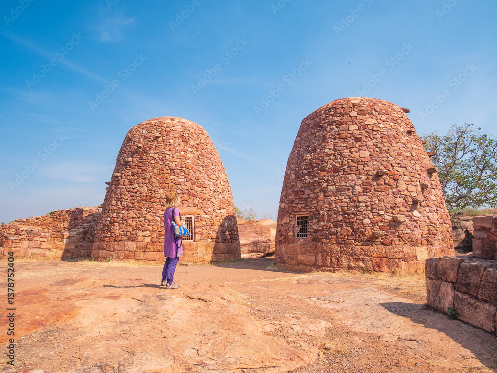 Woman exploring ancient temple site at Badami. Tourist walking among ruins stone walls gateways in Karnataka, India