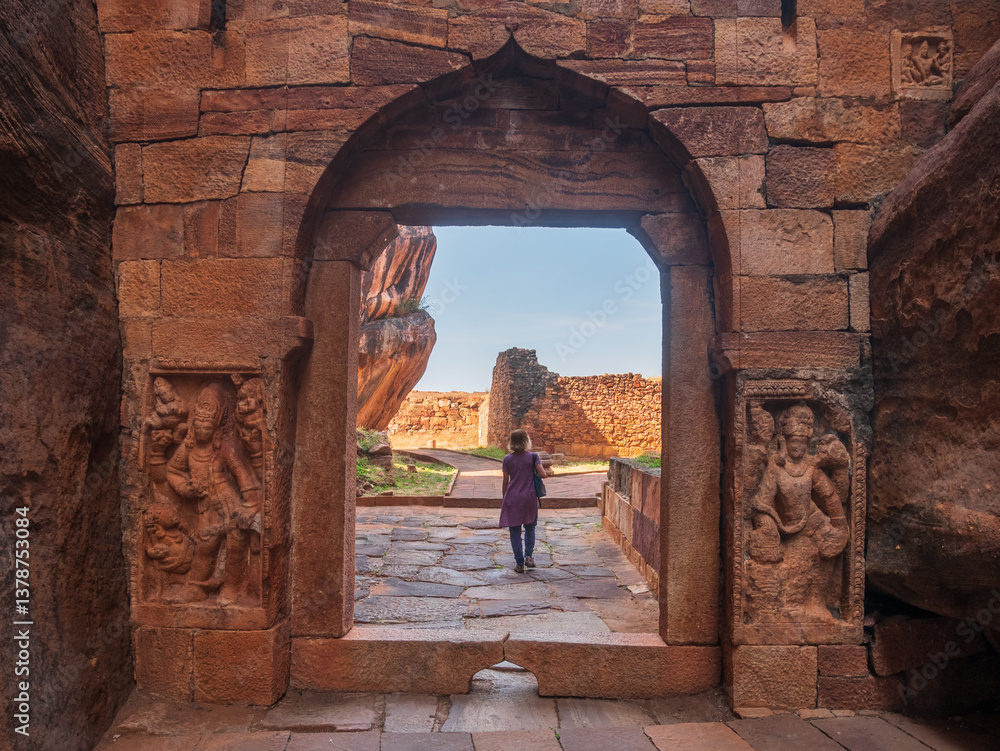 Woman exploring ancient temple site at Badami. Tourist walking among ruins stone walls gateways in Karnataka, India