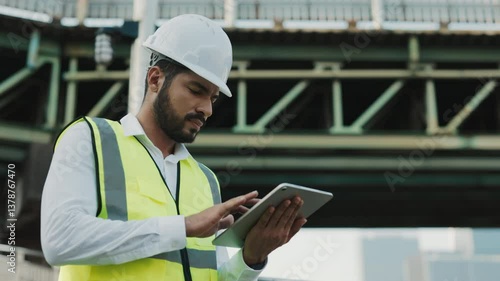 Portrait of thoughtful architect designer working on tablet computer standing near bridge. Inspired man engineer uses portable computer to control at construction site. Copy space