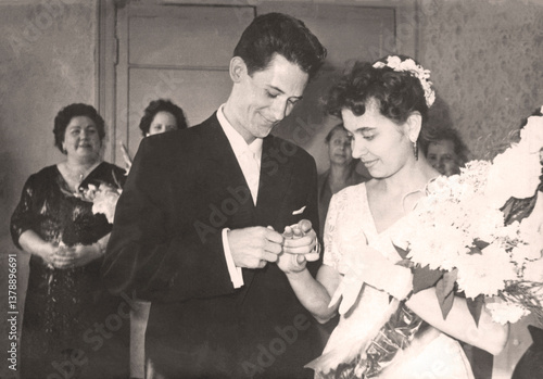 Chasov Yar, USSR - circa 1960: Vintage portrait of the bride and groom. The groom puts a ring on the bride at the registry office. Retro photo.