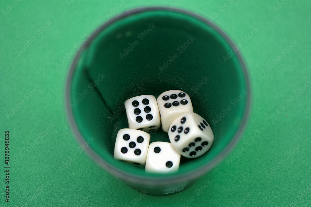 Various white dice with black dots resting inside a green cup se