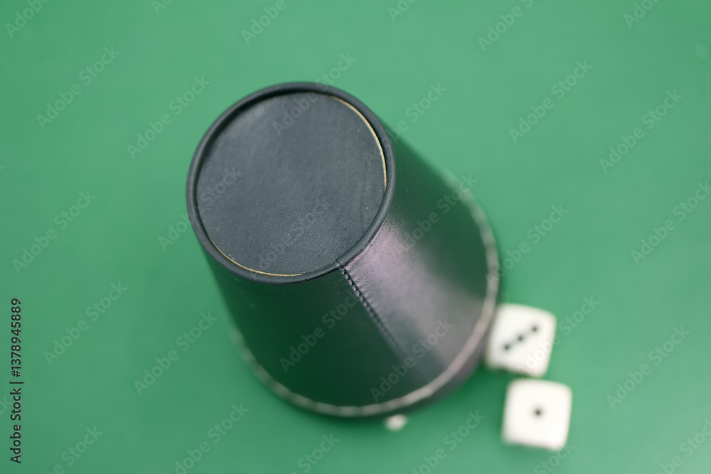 Dice covered by a black cup on a green surface ready for a game
