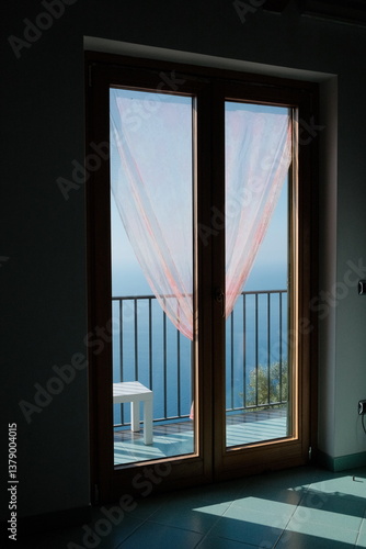 Wallpaper Mural Soft sunlight filters through sheer curtains of a hotel room on the Amalfi Coast, revealing a balcony view of the blue sky, distant ocean, and serene morning horizon. Torontodigital.ca