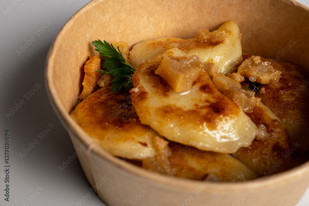 Fried dumplings with golden crust and crispy pork cracklings in a kraft paper bowl. Traditional Eastern European food, close-up, delicious street food concept