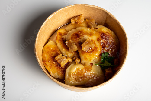 Fried dumplings with golden crust and crispy pork cracklings in a kraft paper bowl. Traditional Eastern European food, close-up, delicious street food concept